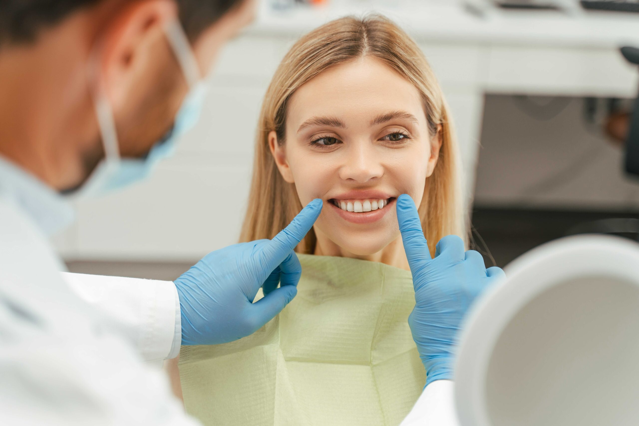 Smiling woman looking in mirror, checking her teeth in modern dental clinic. Health care concept